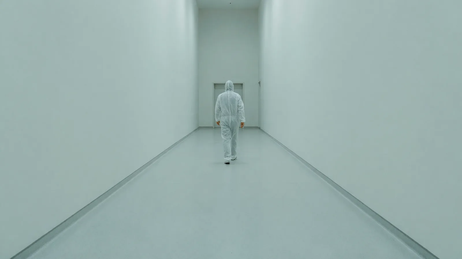 A plant worker in white coveralls walks a long clean corridor — the NRC's ALARA rewrite leads today's brief. Illustration: NNN