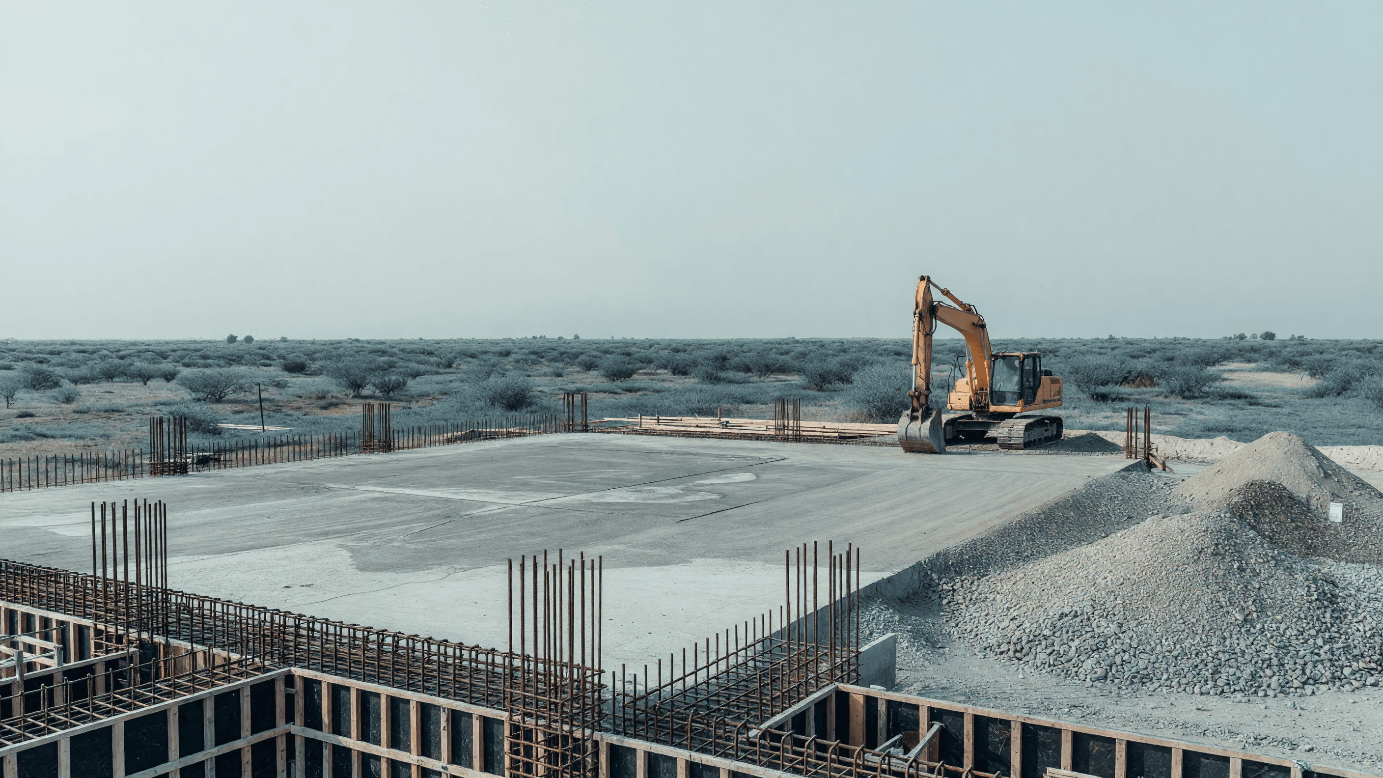A concrete construction pad with rebar and an excavator at the Mahi Banswara nuclear project site — India's PHWR procurement leads today's brief. Illustration: NNN