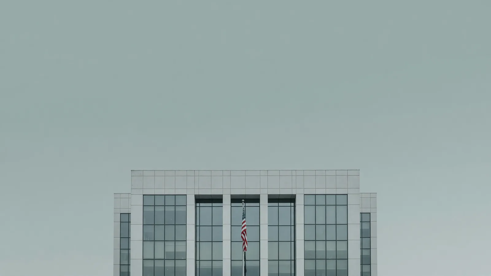 A federal regulatory office building behind a single US flag — the NRC's NEPA streamlining proposal. Illustration: NNN