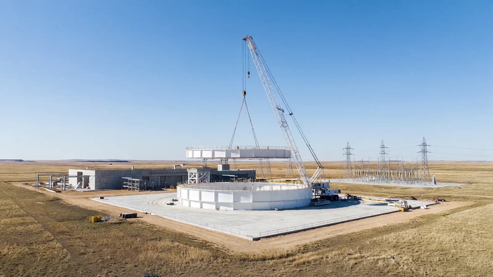 A white steel containment ring for a pressurized-water reactor being lifted by a heavy-lift crane onto a concrete pad at a US nuclear construction site on open prairie, representing the up-to-eight-reactor US build program South Korea is finalizing to power AI data centers. Illustration: NNN