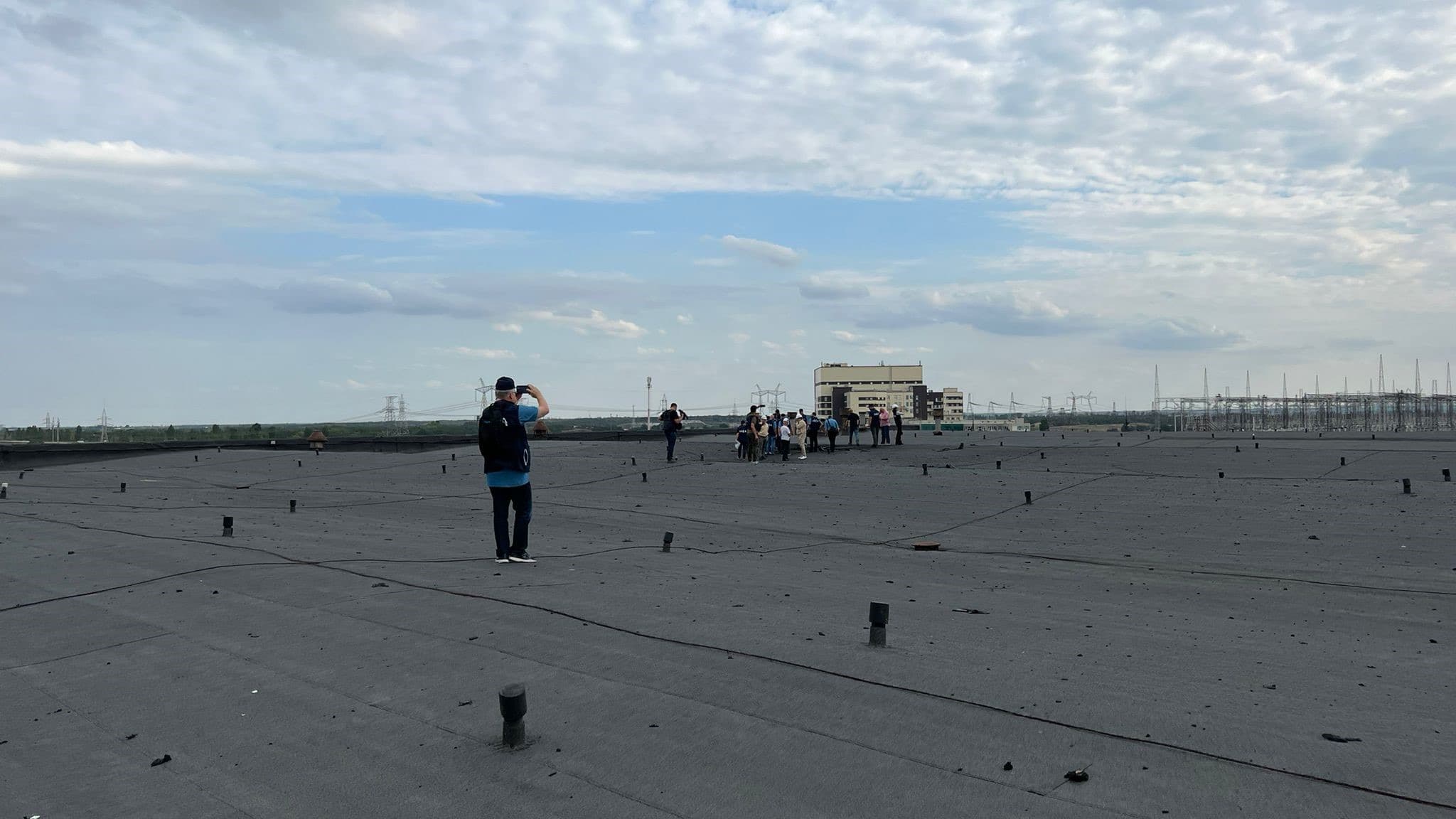 An IAEA monitoring team stands on a rooftop at the Zaporizhzhya Nuclear Power Plant, overlooking the plant buildings and the high-voltage switchyard where the repaired 330 kV Ferosplavna-1 line reconnected the plant to Ukraine's grid. Image: IAEA Imagebank (CC BY 2.0)