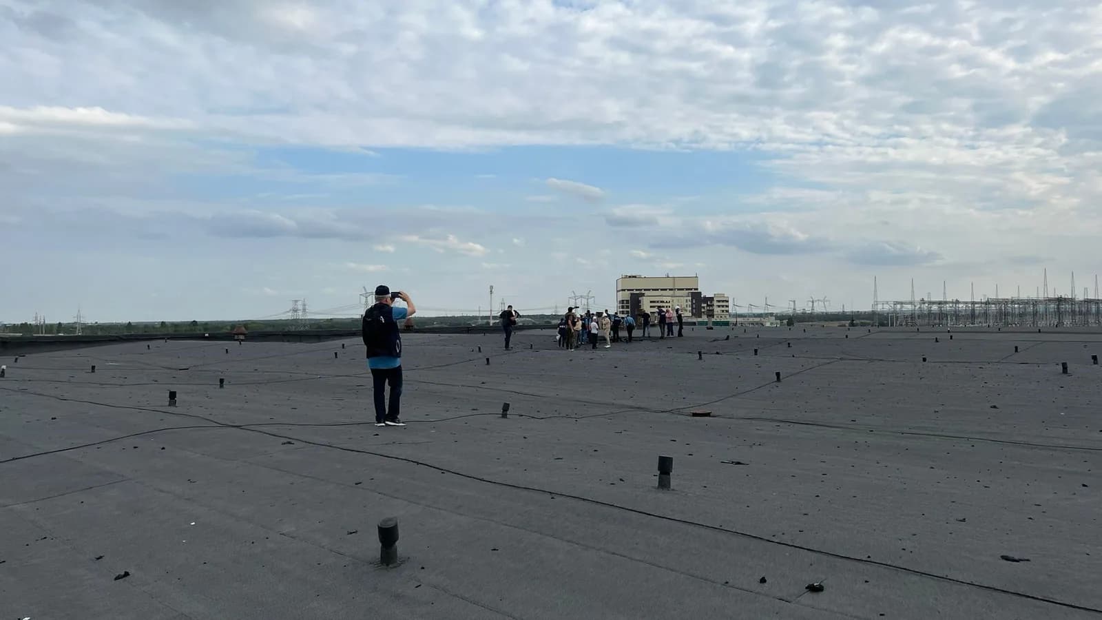 An IAEA monitoring team stands on a rooftop at the Zaporizhzhya Nuclear Power Plant, overlooking the plant buildings and the high-voltage switchyard where the repaired 330 kV Ferosplavna-1 line reconnected the plant to Ukraine's grid. Image: IAEA Imagebank (CC BY 2.0)